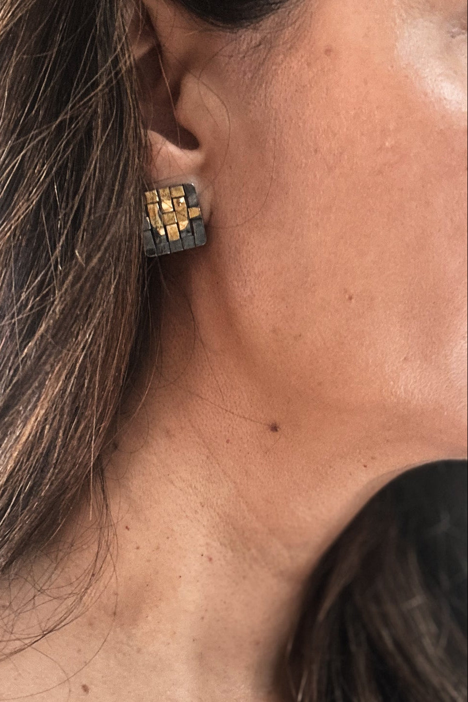 Close-up of an ear wearing a geometric gold and black earring.
